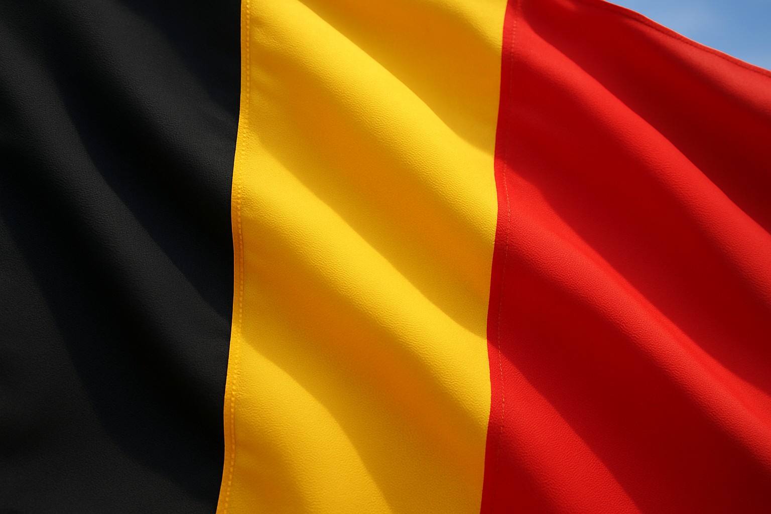 Die belgische Nationalflagge mit den vertikalen Streifen Schwarz, Gelb und Rot weht im Wind, Nahaufnahme mit klar sichtbarer Stofftextur.